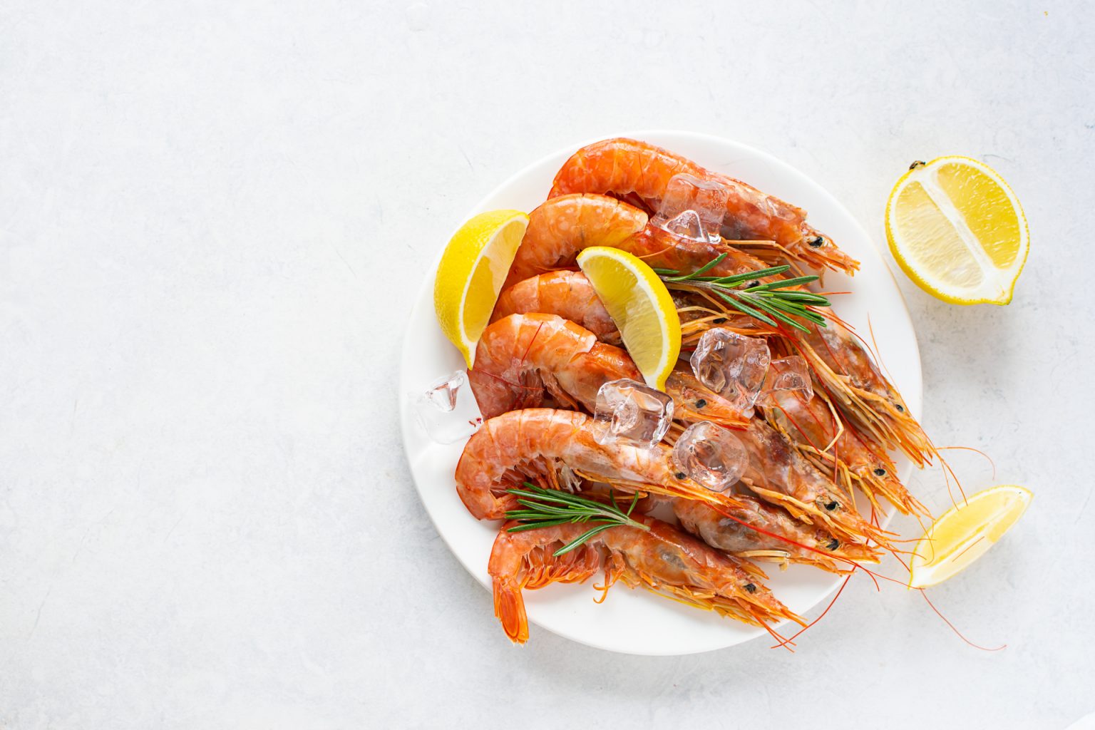 Fresh tiger shrimps or prawns with lemon, herbs and ice on white marble table top view.